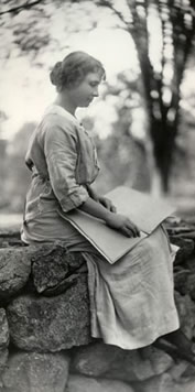 Helen sitting on a stone wall reading braille, 1902