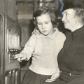 Helen Keller and a young girl sitting in front of a large cabinet radio