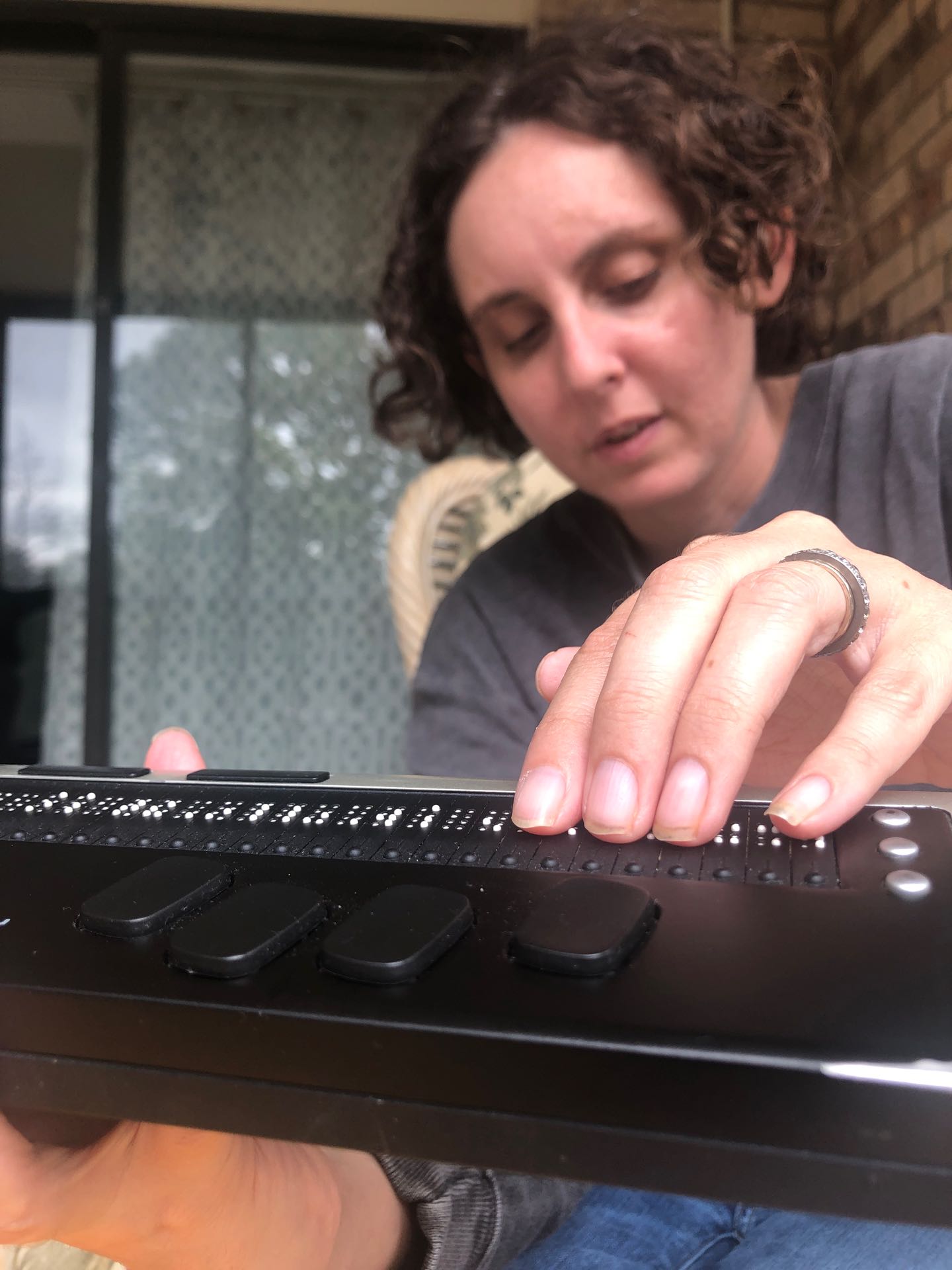 A white woman with short curly brown hair, with her hand on a braille reader