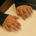 Close-up of child's hand reading brailled book
