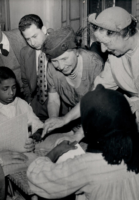  Polly guides Helen's hand to a book in braille. The book is being read by a Lebanese child who is blind, 1952.