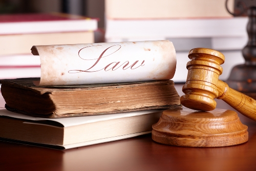 Judge's wooden gavel with old books and paper with word 'law' in background.