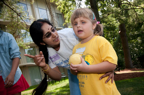 An instructor helps a young girl in playing a sports game outdoors.