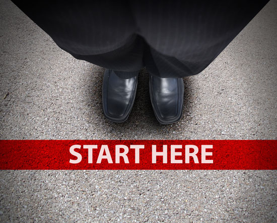 Business man looking down at his feet with a red race line reading 'start here.' 