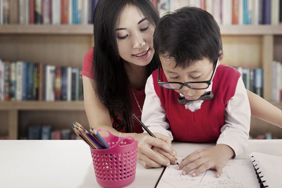 Elementary school student learning to write with his teacher in the library. 