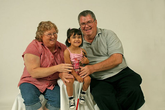 Little girl holding her white cane, sitting with her parents.