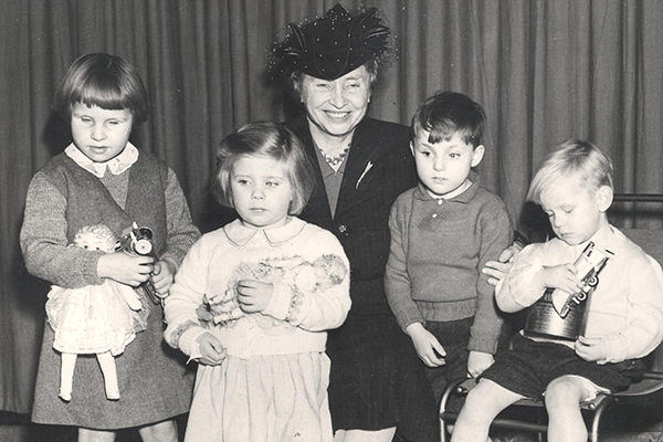 Helen kneels with four children who are all holding toys