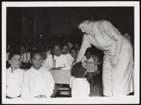 Photograph taken indoors of Helen Keller with a class of school children at the Dominican School for Colored Deaf, South Africa.