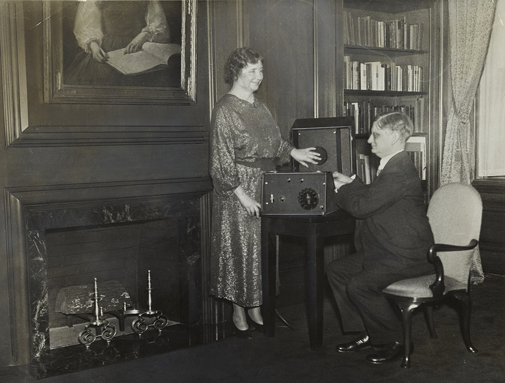 Helen Keller, standing to the left, and Robert B. Irwin, seated to the right, using a Talking Book Machine.
