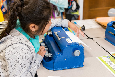young female student taking embossing paper from a braille writer. 