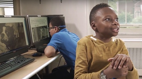 Two fifth-grade students sit at a table with computers exploring the digital Helen Keller Archive. Student in background is viewing monitor; student in foreground is turned around in his chair discussing his findings.