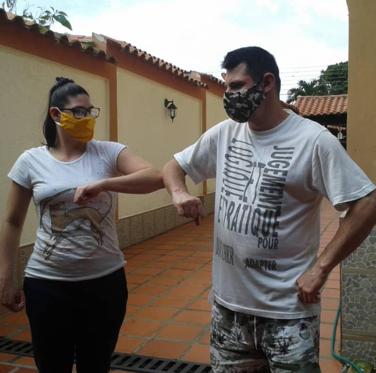 Two young Latinx people wearing masks bump elbows in greeting.