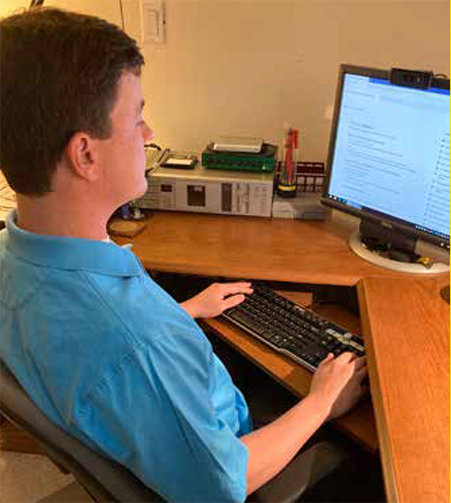 A middle-aged White man sits at a computer. His right hand is typing on the number pad by the keyboard.