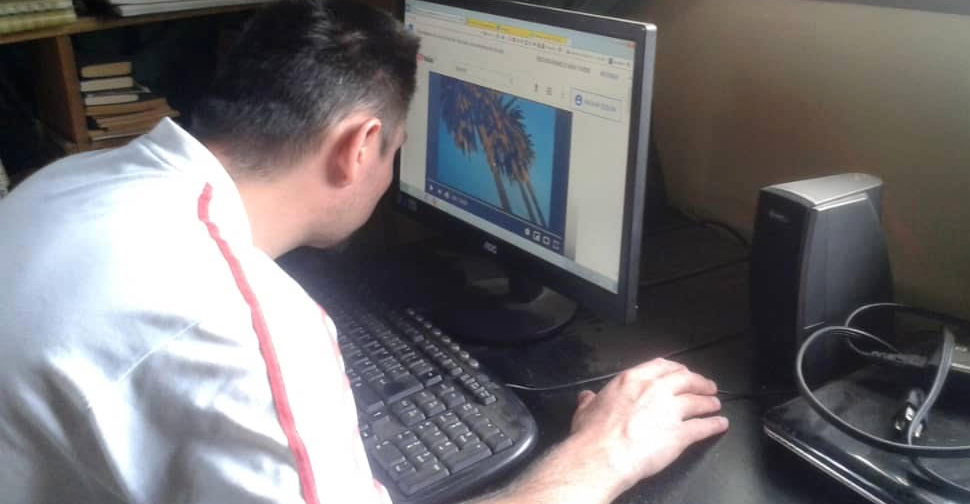 A Latinx man at a desk leans in to look at an image on a computer screen.