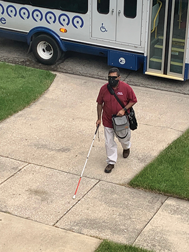 An Indian man uses a white cane after exiting a paratransit van. 