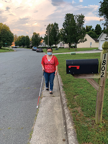 A young woman walks down a sidewalk with her white cane.