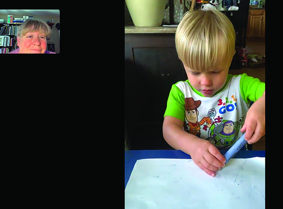 A white toddler colors with a blue crayon as a White TVI watches remotely. 
