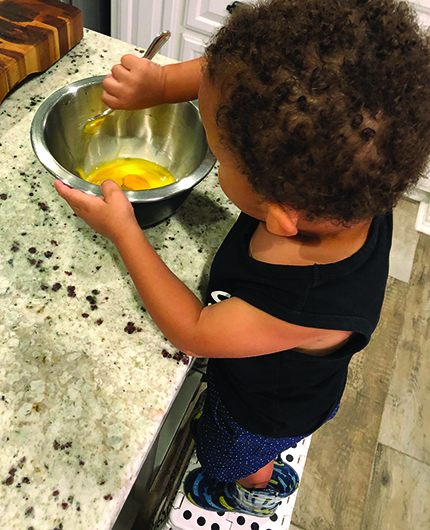 A Multiracial boy whisks eggs in a metal bowl.