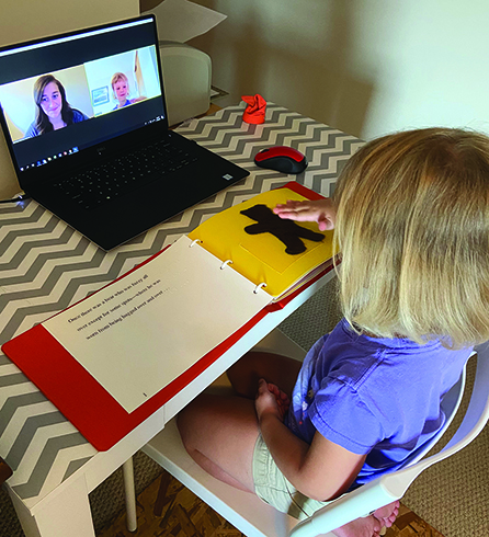 A White preschool girl explores the teddy bear in the book "That's Not My Bear" with the TVI watching remotely on the computer screen. 