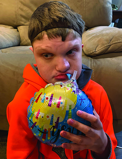 A White young adult deafblind student sits on the floor holding a Mylar balloon. 
