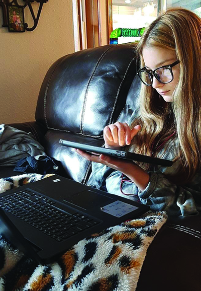 A White middle school girl with low vision participates in online learning from the comfort of her couch. 