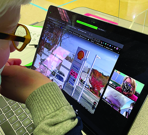 A White elementary school-aged boy with albinism is in a Zoom meeting with his White female O&M specialist. They are a looking at the street view of Google Maps. A gas station is visible. 