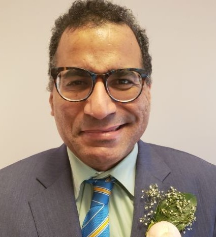 Marc Safman headshot. A man in a gray suit and glasses, smiling.
