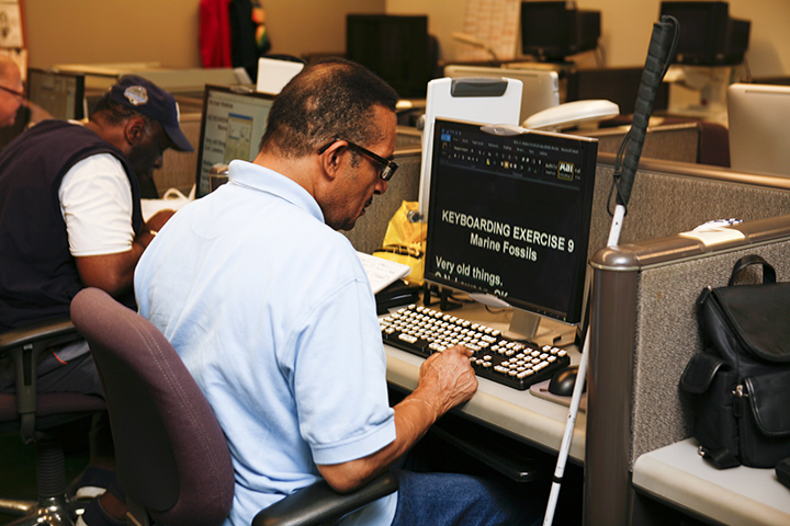 View from behind, a man reads from a computer with large text on the screen