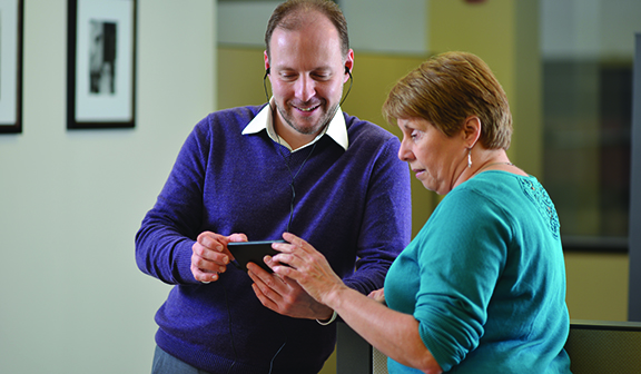 A man wearing earbuds and a woman stand together with a cell phone