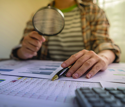 Person holding a magnifying glass over an array of papers