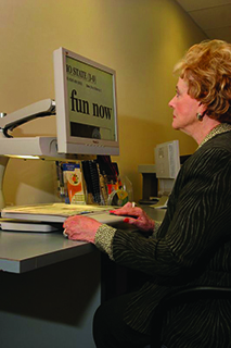 Profile of a woman with light skin and light brown hair reading text using a closed circuit TV (CCTV)