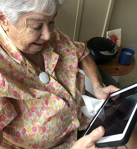 An older woman is pictured sitting and looking at a tablet device. 