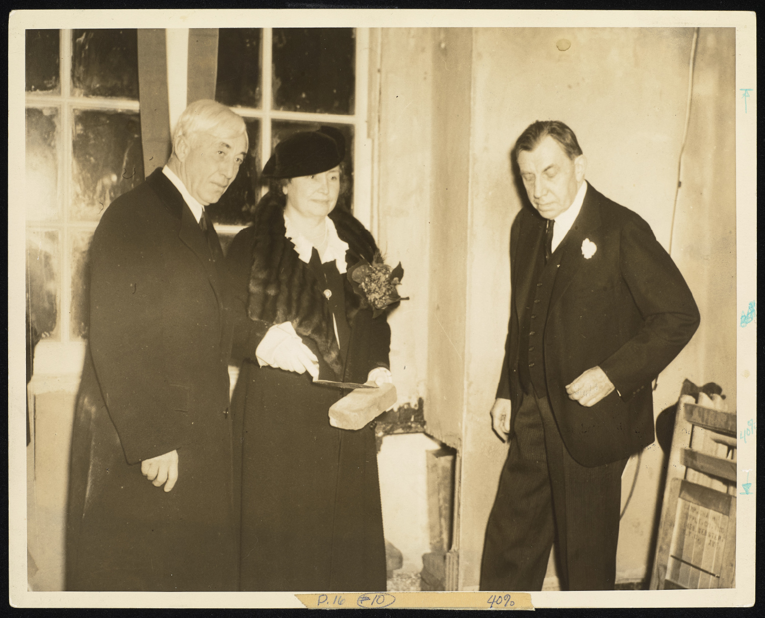 M. C. Migel, Helen Keller, and Dr. John Finley stand in a room that looks as if it's still under construction. Migel and Keller hold a trowel, and Keller also holds a brick.