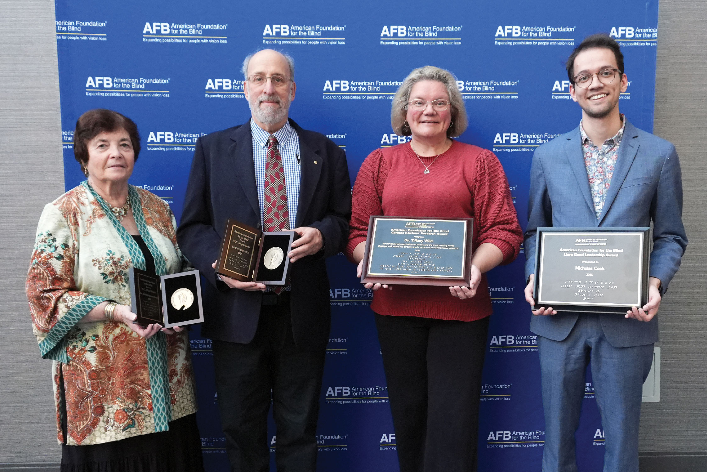 A group of four individuals in front of an AFB banner, smiling and proudly holding their awards.