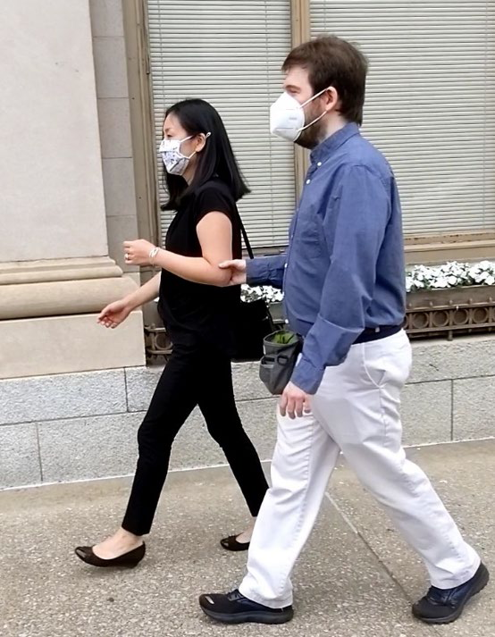 A young man lightly holding onto a woman's arm just above the elbow. The woman walks slightly in front of him.
