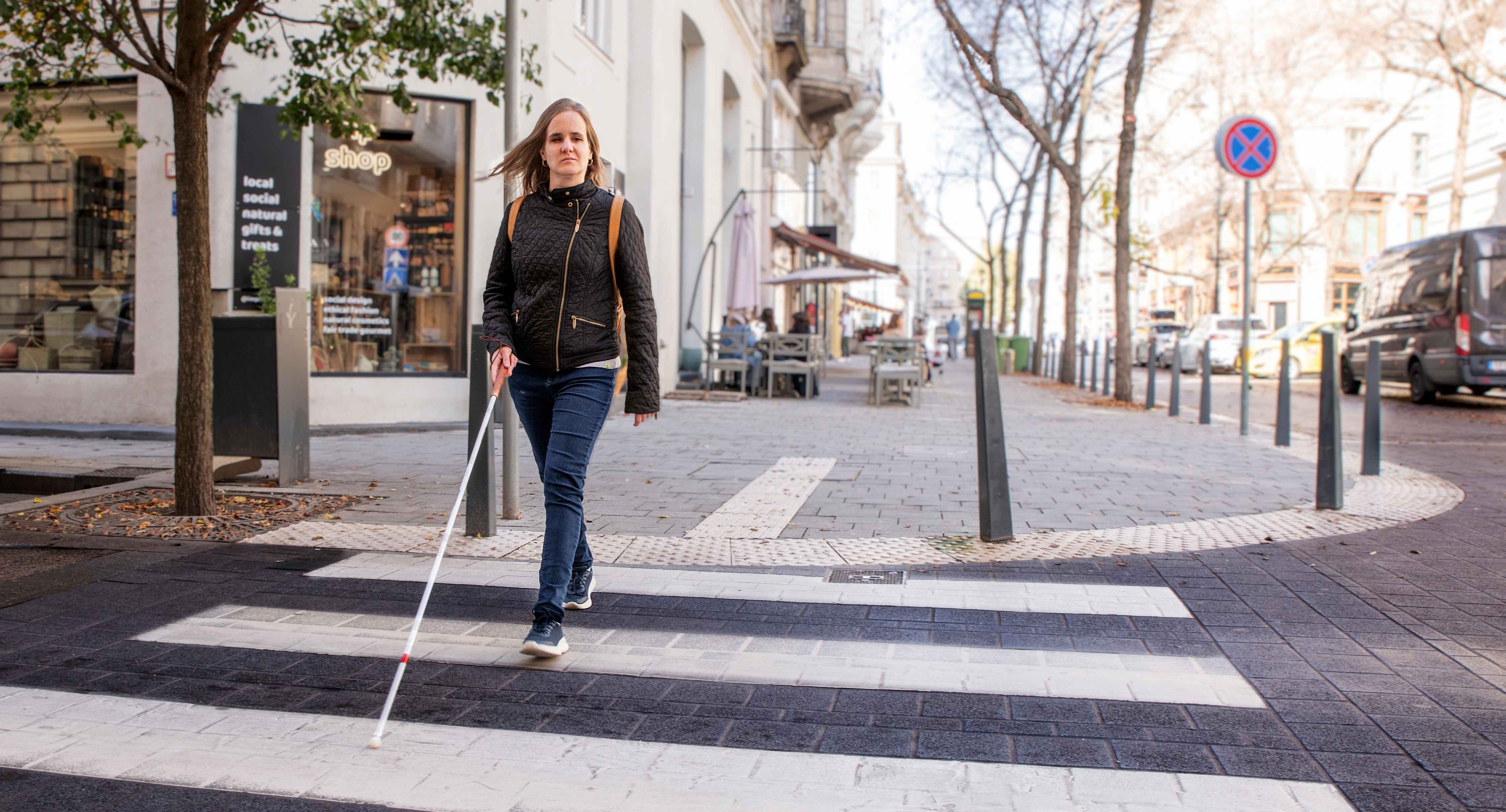 A woman uses a white cane while crossing a street.