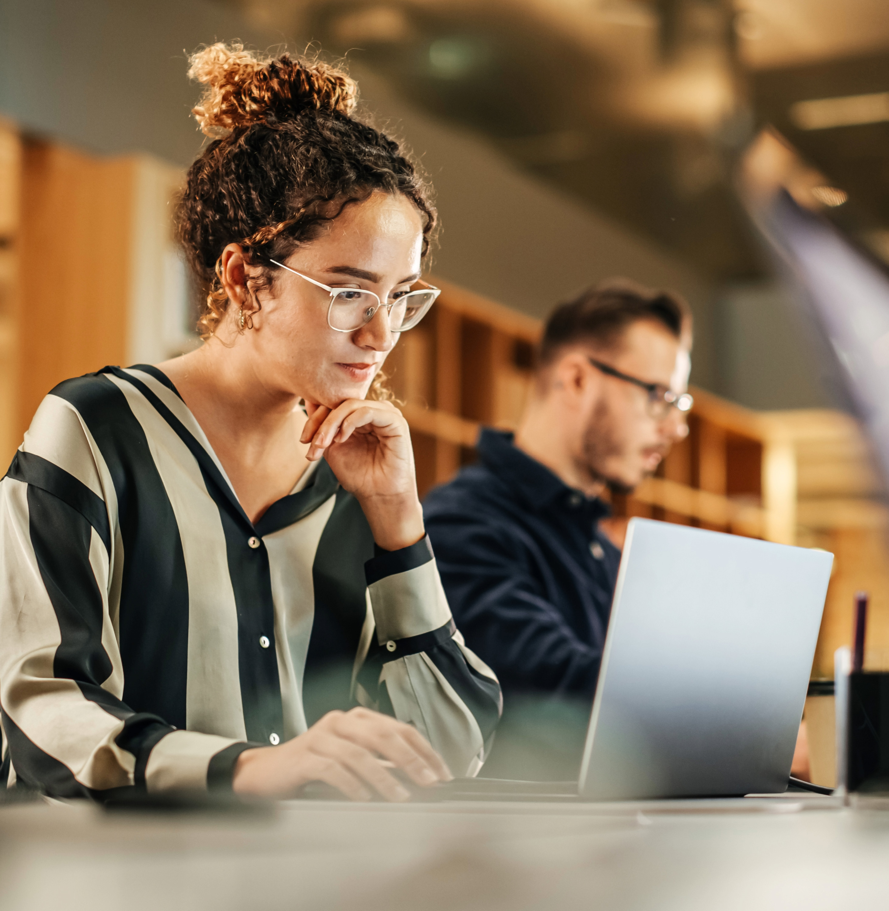 A woman and a man sit at an office table and work on their computers.