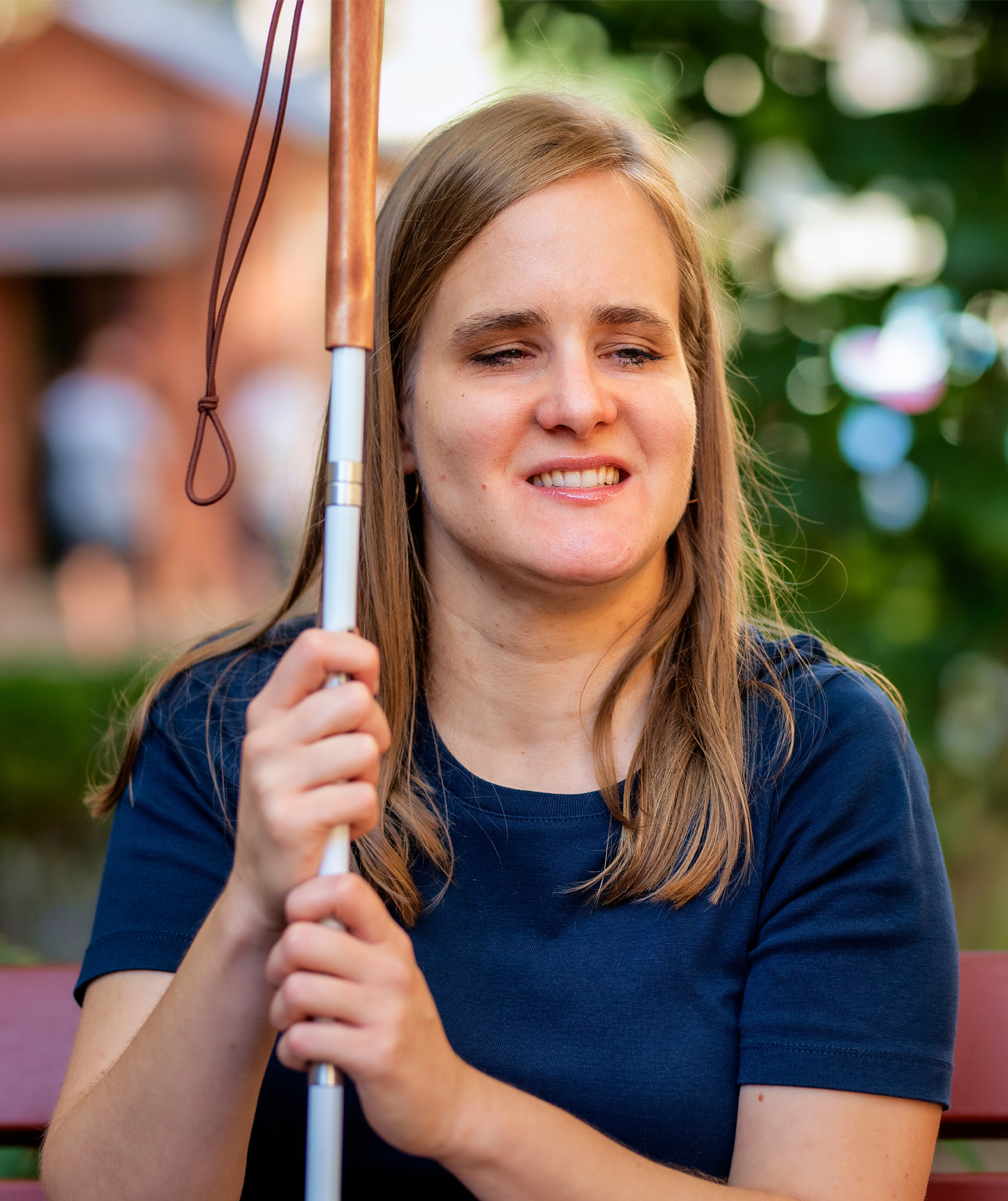 A woman sits outside, holding her white cane.