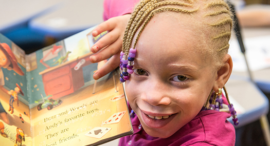 visually impaired girl smiling at camera, holding up a book