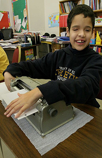 Un muchacho sonriente utiliza un escritor braille en su salón de clases