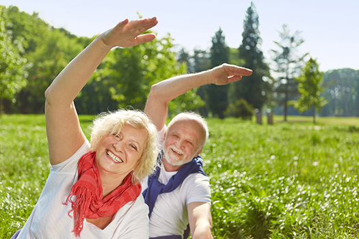 senior man and woman stretching their arms over their heads, smiling