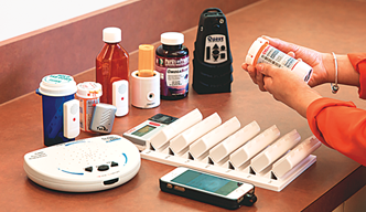 A woman holding a cell phone in her hand. A variety of medications are on a table in front of her.