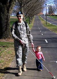 Man in a military uniform walking with a long mobility cane holding his small daughter's hand