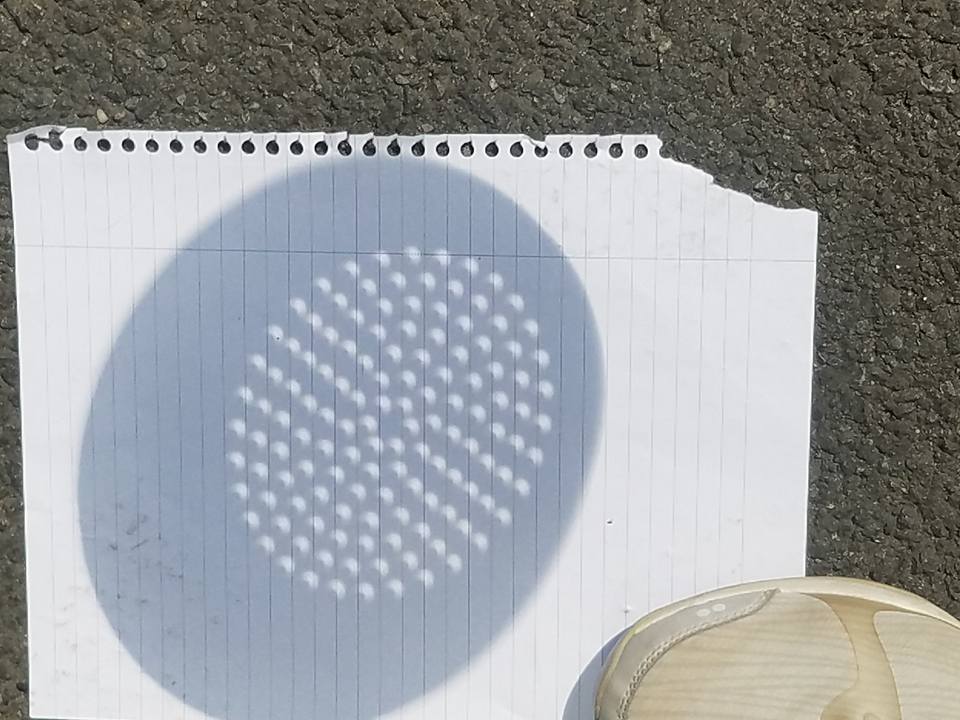 The shadow cast by a colander during the solar eclipse -- each hole in the colander reveals a crescent shape on the white piece of notepaper.