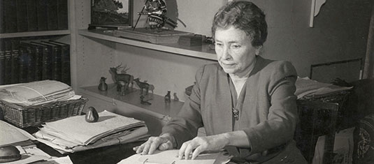 Helen Keller reading braille at her desk