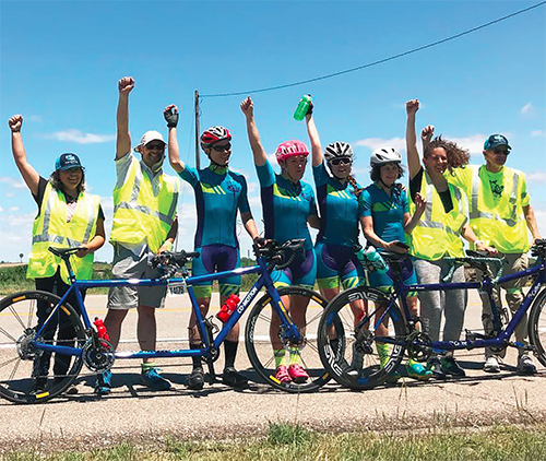 Team Sea to See stands behind their tandem bikes with arm upraised in victory.