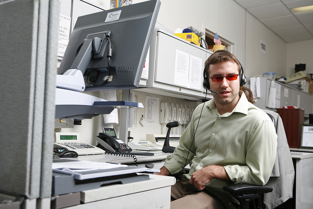 Young man sitting at cubicle desk wearing headset.