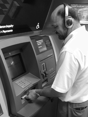 Figure 3: Photograph of a man wearing a headset receiving cash from the slot under the keypad of a Chase e-ATM.