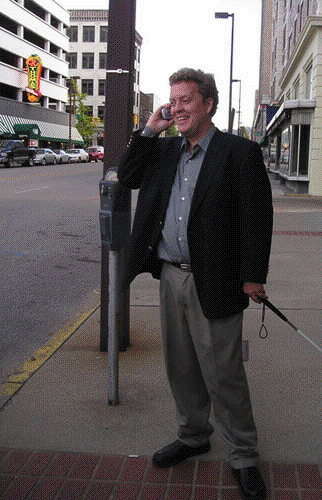 A pleased-looking man stands on a street corner talking on his cell phone.