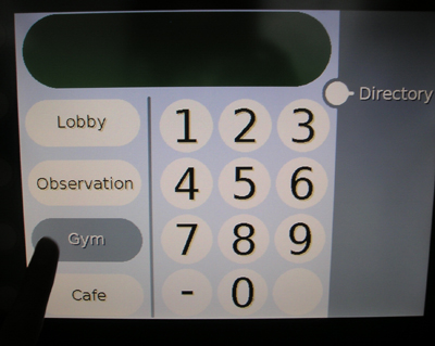 Photo of a touch screen with buttons along the left side labeled Lobby, Observation, Gym, and Cafe. A finger is touching the button labeled Gym, which is highlighted.